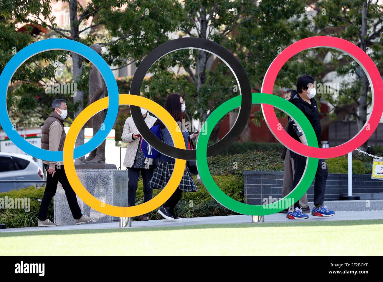 people-wearing-facemasks-are-seen-behind-the-olympic-symbols-of-the