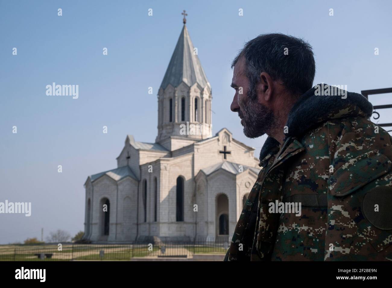 SHUSHI, NAGORNO KARABAKH - NOVEMBER 03: An ethnic Armenian wearing a military fatigue stands in front of the Armenian Apostolic Holy Savior Cathedral commonly referred to as Ghazanchetsots during a military conflict between Armenian and Azerbaijani forces over the disputed Nagorno-Karabakh region known also as the Artsakh Republic in the town of Shushi or Shusha in the self-proclaimed Republic of Artsakh or Nagorno-Karabakh, de jure part of the Republic of Azerbaijan on November 03 2020. The fighting between Armenia and Azerbaijan over Nagorno-Karabakh known also as the Artsakh Republic re-eru Stock Photo