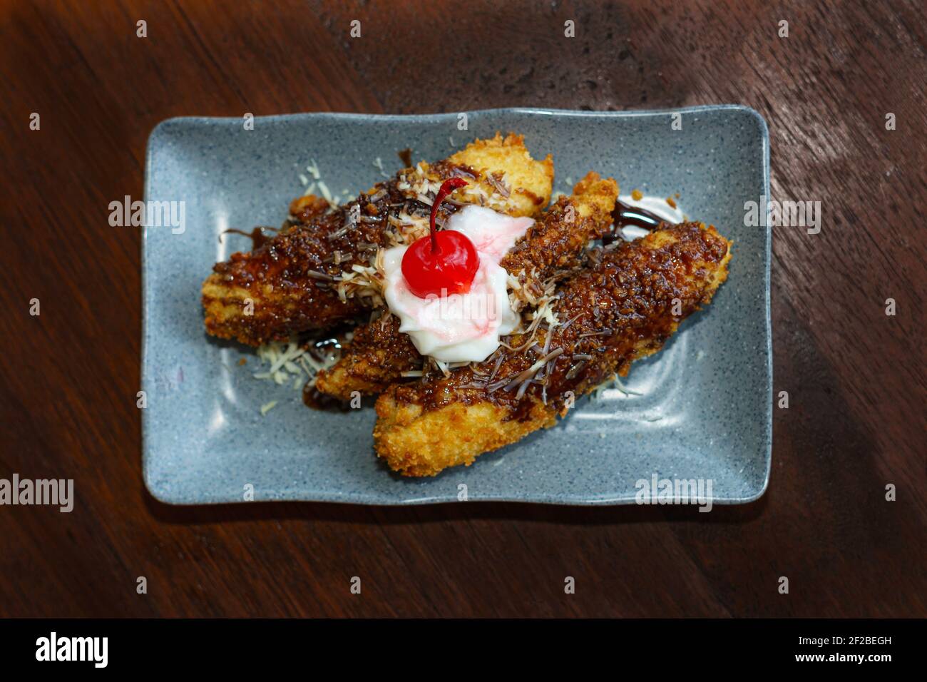 Fried bananas with buttercream icing and a glace cherry garnish Stock Photo