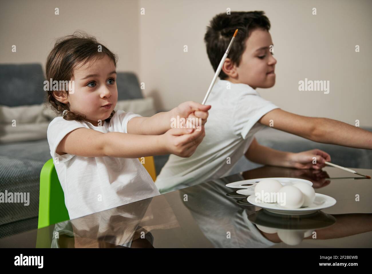 Two charming children holding paintbrushes ready for decorating Easter eggs with paints. Stock Photo
