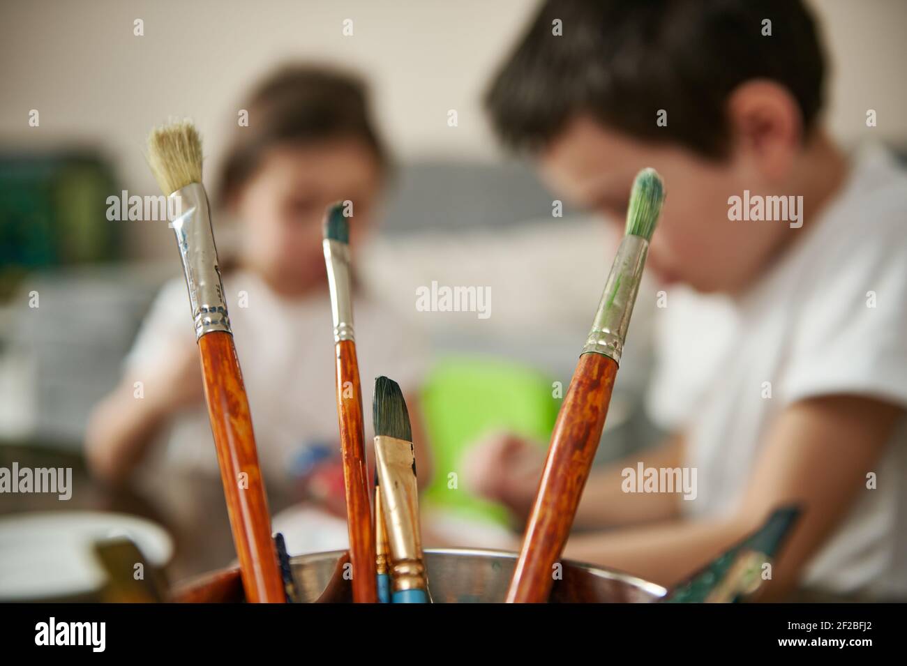 Closeup of different paint brushes on the background of blurred children concentrate on decorating eggs for Easter Stock Photo
