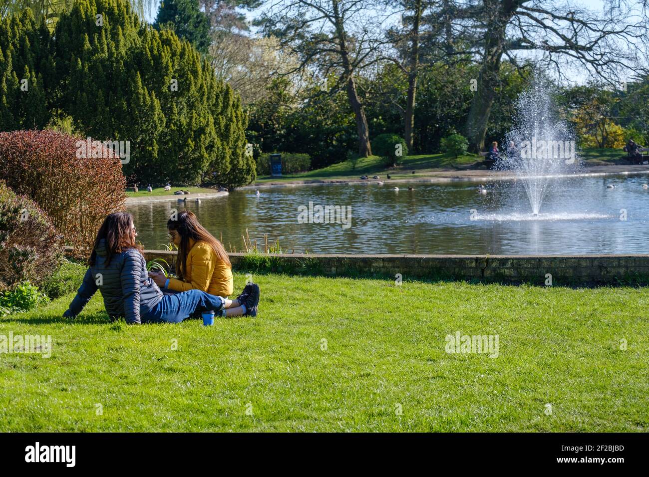 Two ladies sit on the grass, enjoying nature and the pond at Pinner