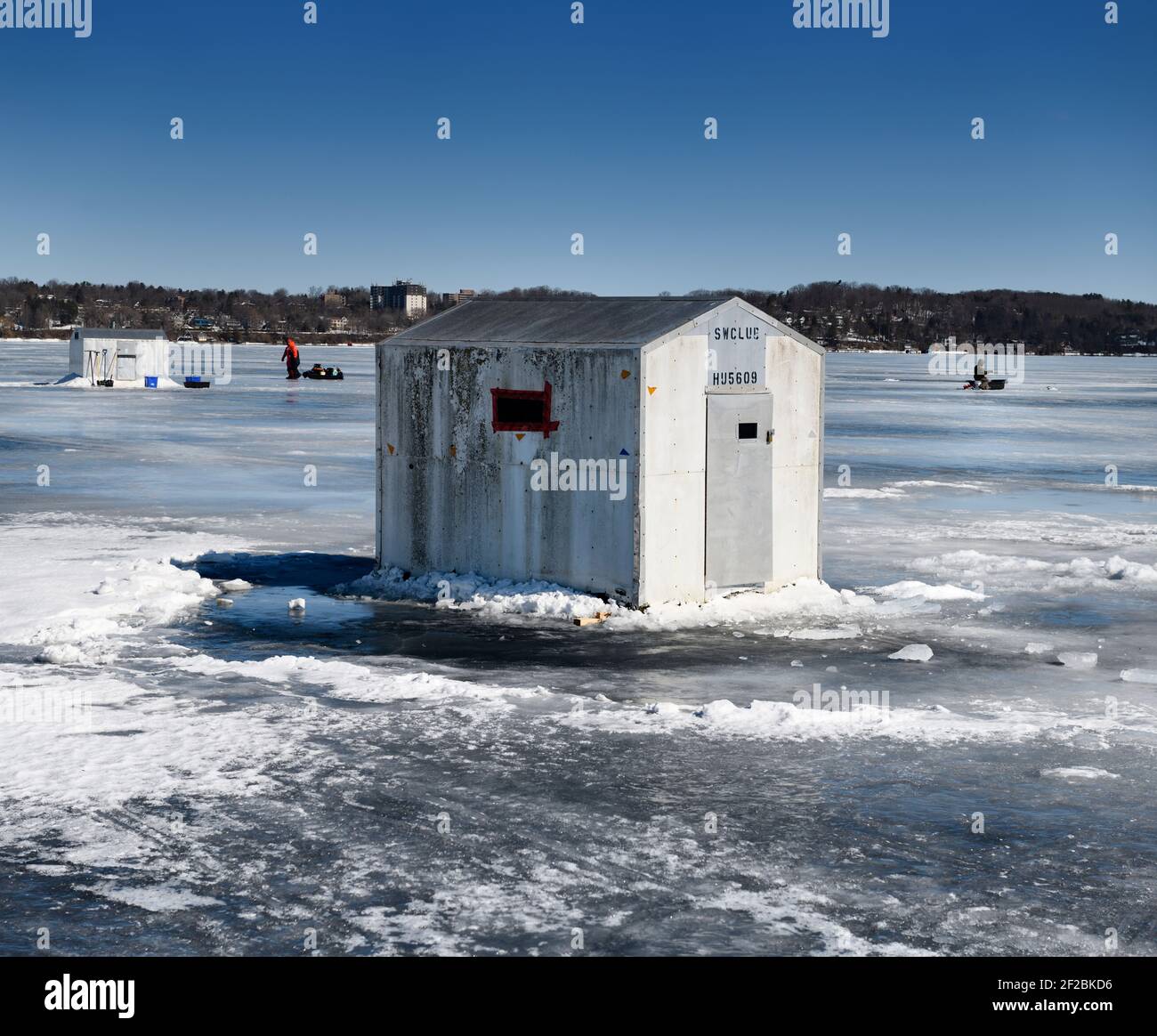Ice fishing shacks on frozen Kempenfelt Bay of Lake Simcoe in winter with fishermen fishing and hauling a sled Stock Photo