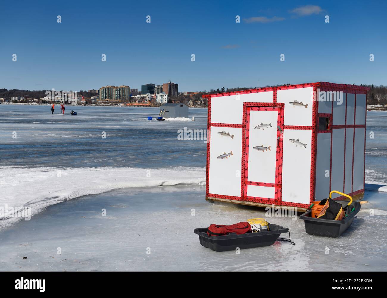 Ice fishing shack with sleds and fishermen drilling hole on frozen