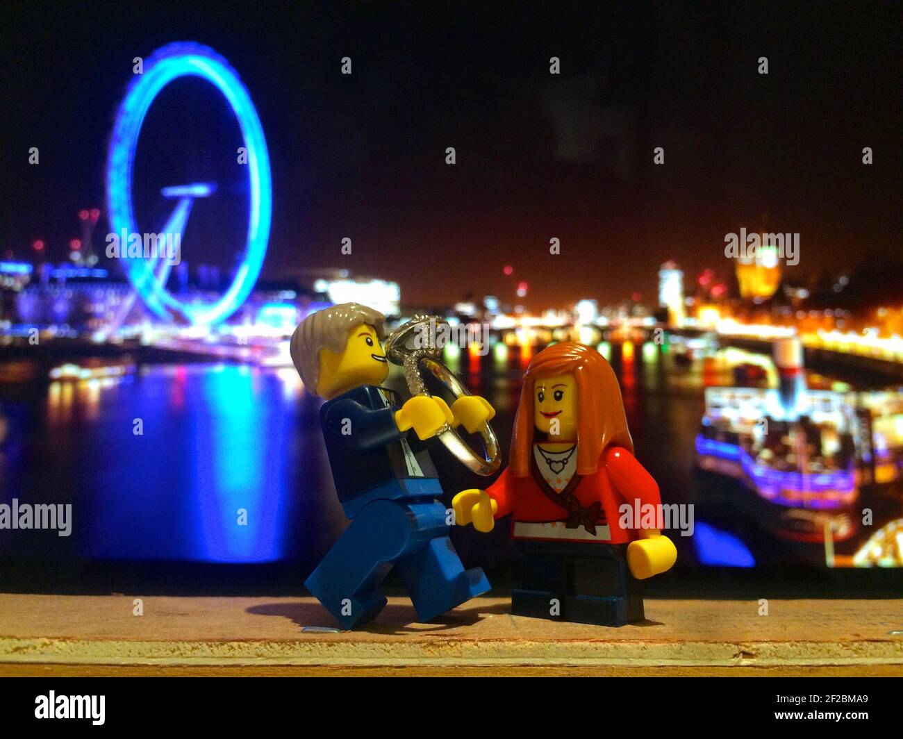 Lego man proposes to lego woman with giant wedding ring in front of London Eye Stock Photo