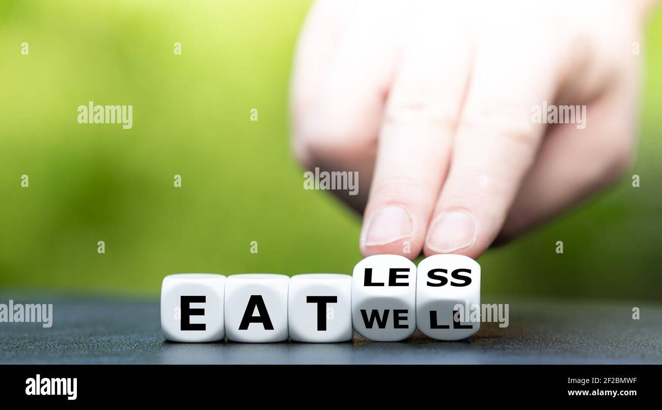 Hand turns dice and changes the expression 'eat well' to 'eat less'. Stock Photo