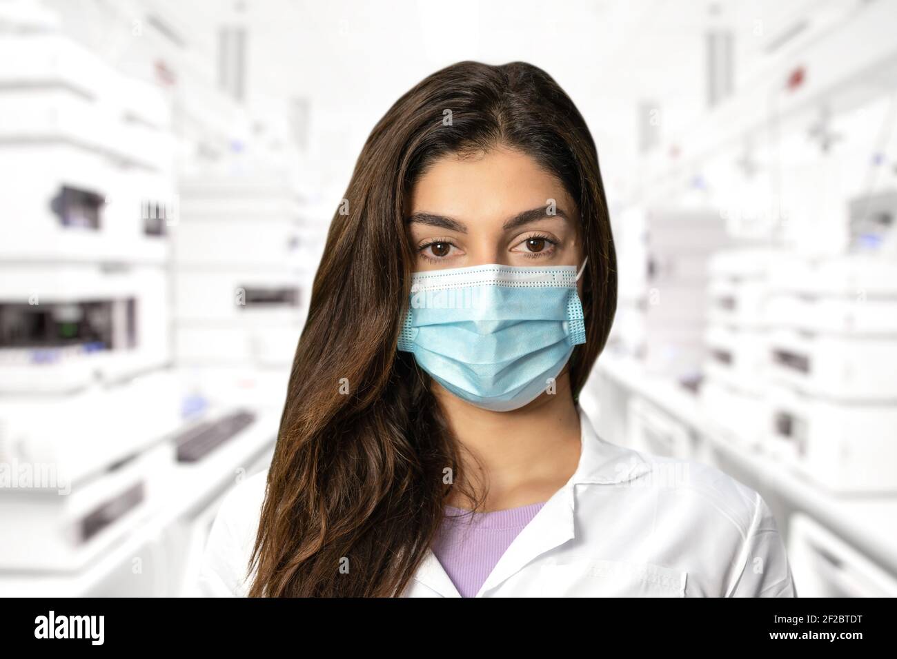 A scientific researcher in a surgical gown and mask. In the background the blurred medical laboratory. Perfect shot for pandemic, research, vaccine an Stock Photo