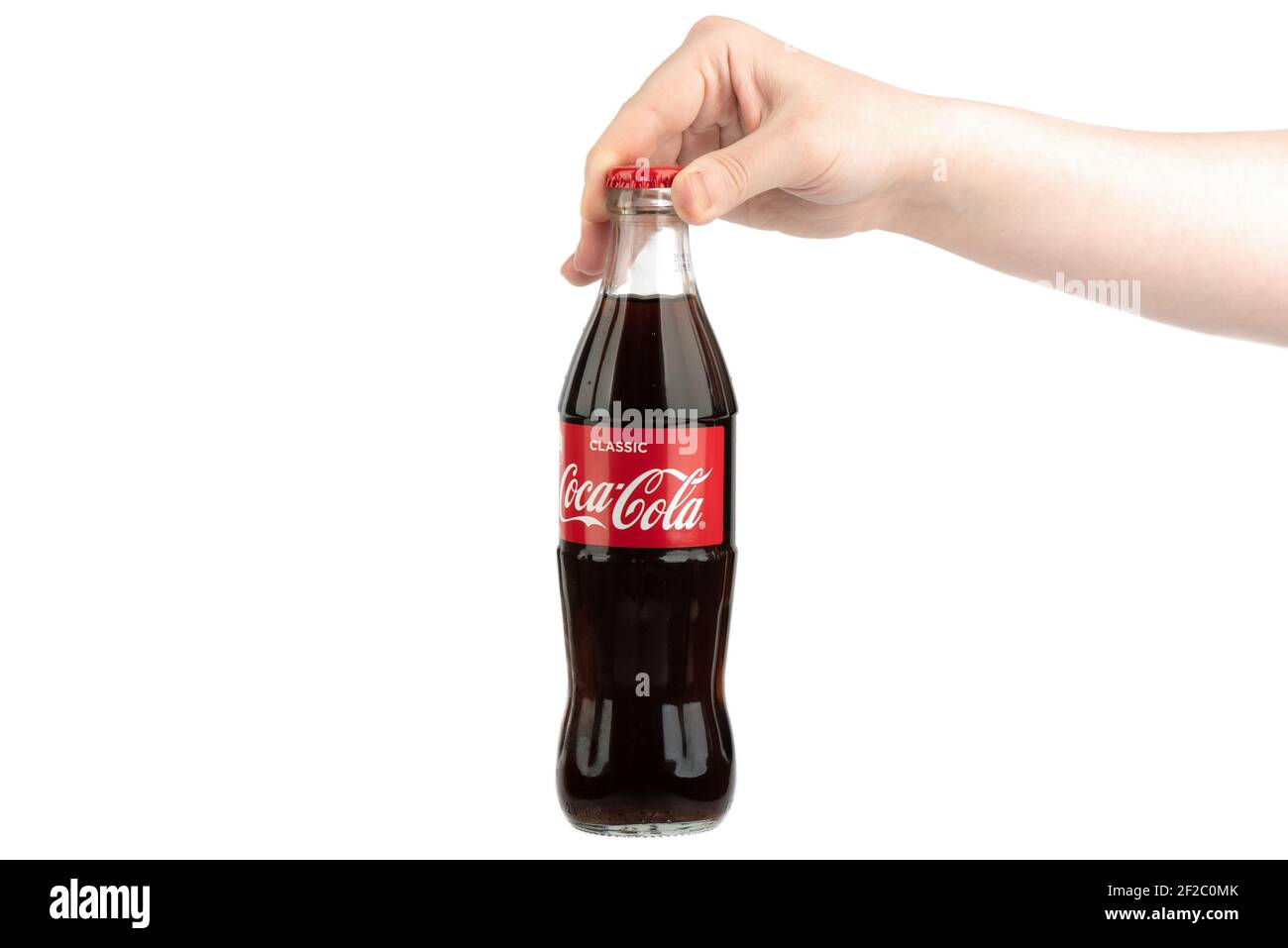 Moscow, Russia - March 1, 2021: A woman's hand holds a glass bottle of Coca-Cola Classic by the cork. Copy space. Stock Photo