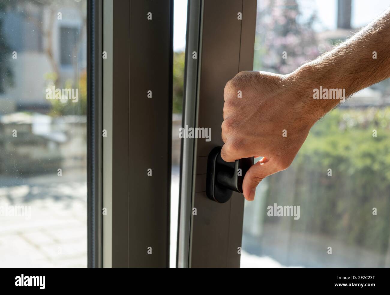 Tilt and turn grey color aluminum window, man holding the handle, fresh air for home. Male hand vertical open metal or PVC window, closeup view. Stock Photo