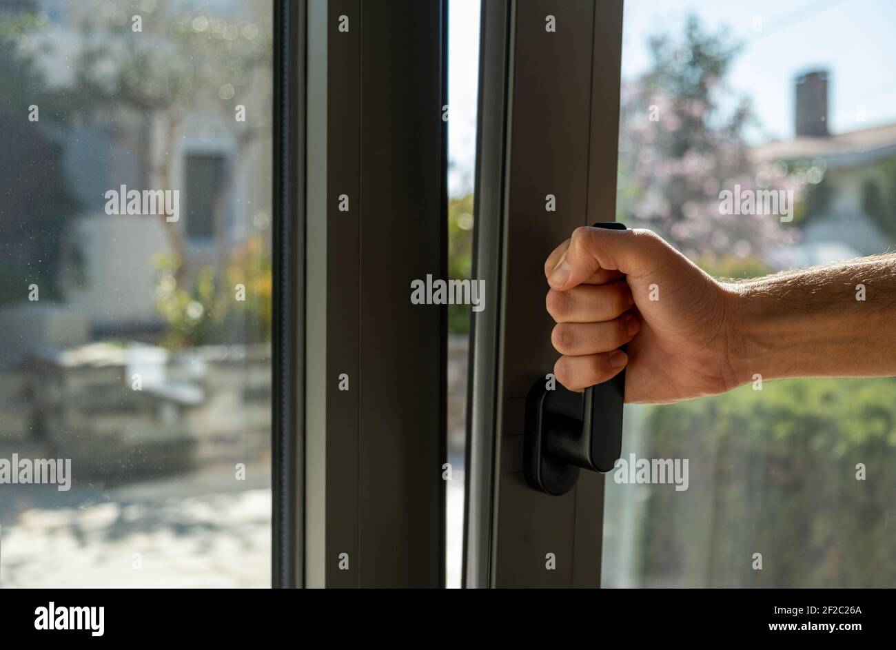 Tilt and turn grey color aluminum window, man holding the handle, fresh air for home. Male hand vertical open metal or PVC window, closeup view. Stock Photo