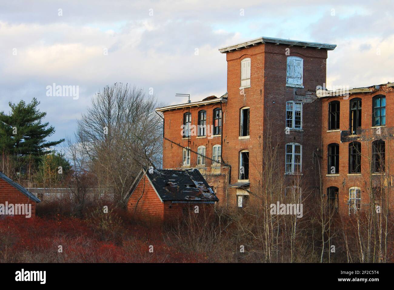 An old, abandoned, brick building that is falling into ruin, with broken windows and overgrown yard. Stock Photo