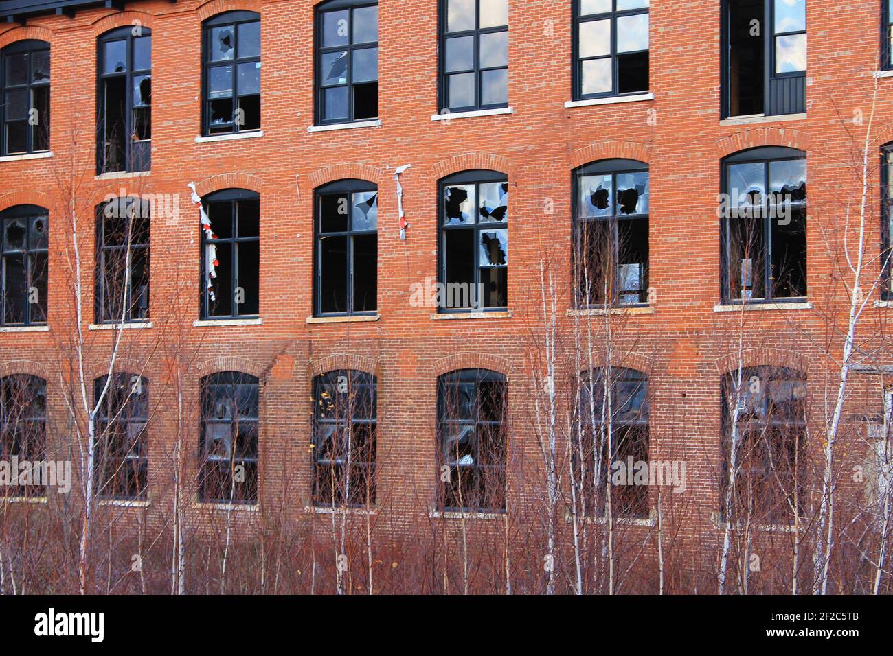 An old, abandoned, brick building that is falling into ruin, with broken windows and overgrown yard. Stock Photo