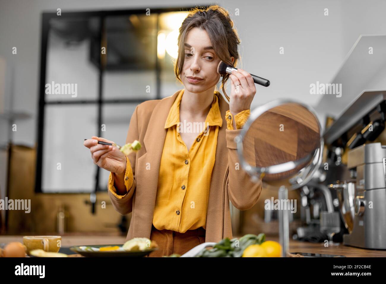 Fussy young businesswoman in a hurry to work in the morning, eating breakfast and apllying makeup on the go Stock Photo