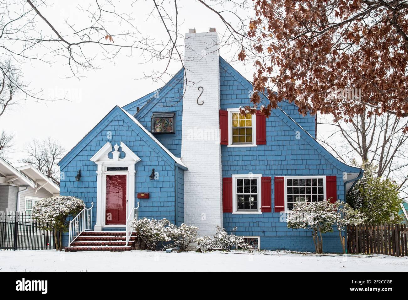 Cute blue painted shingled vintage cottage in the snow with red shutters and white chimney and trim Stock Photo