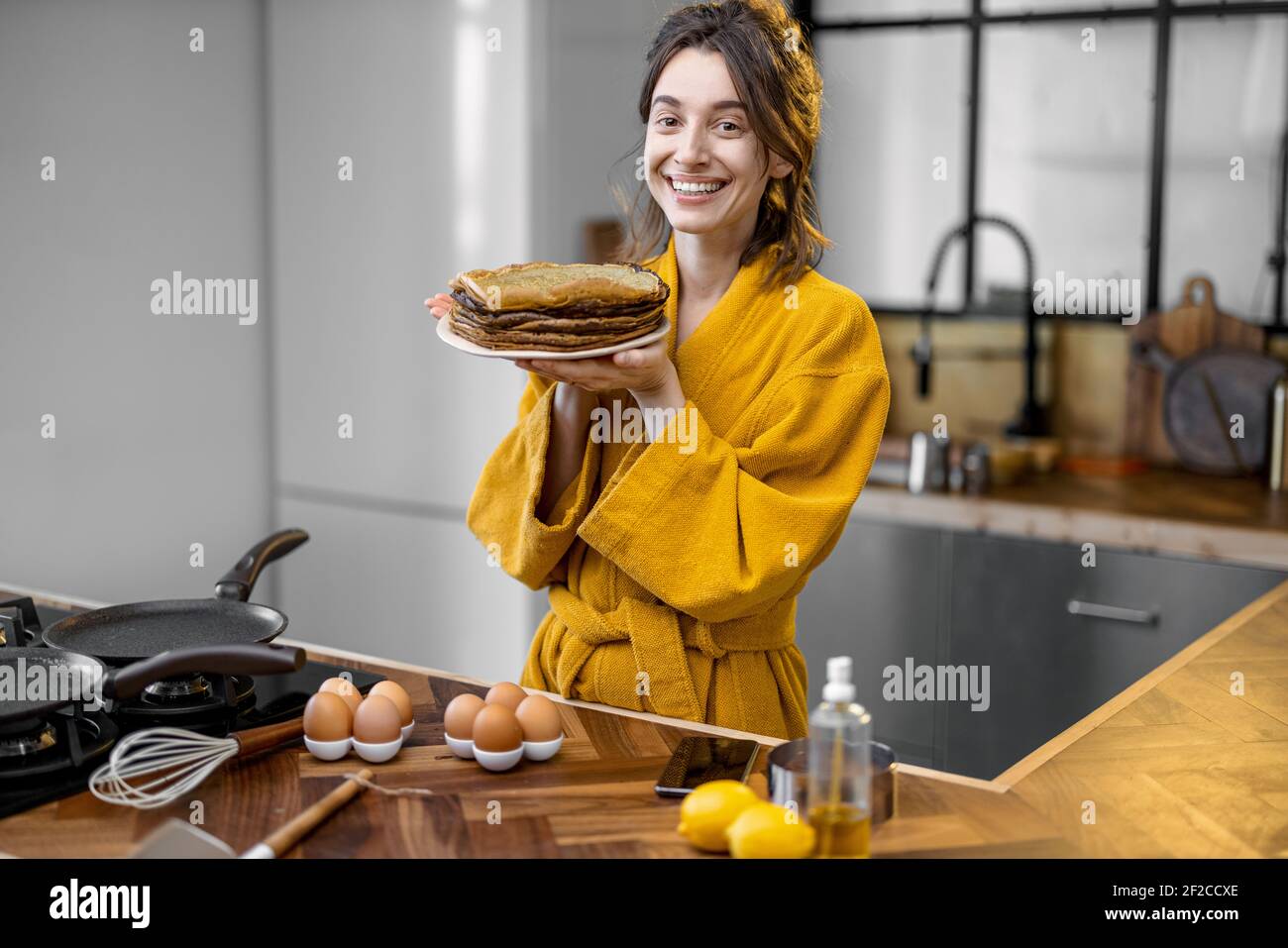 Portrait of a young cheerful housewife dressed in bathrobe with a stack ...