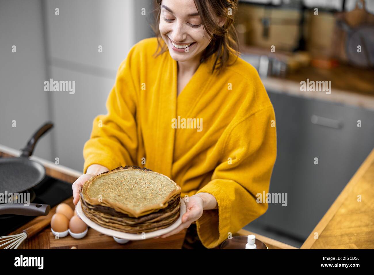 Portrait of a young cheerful housewife dressed in bathrobe with a stack ...