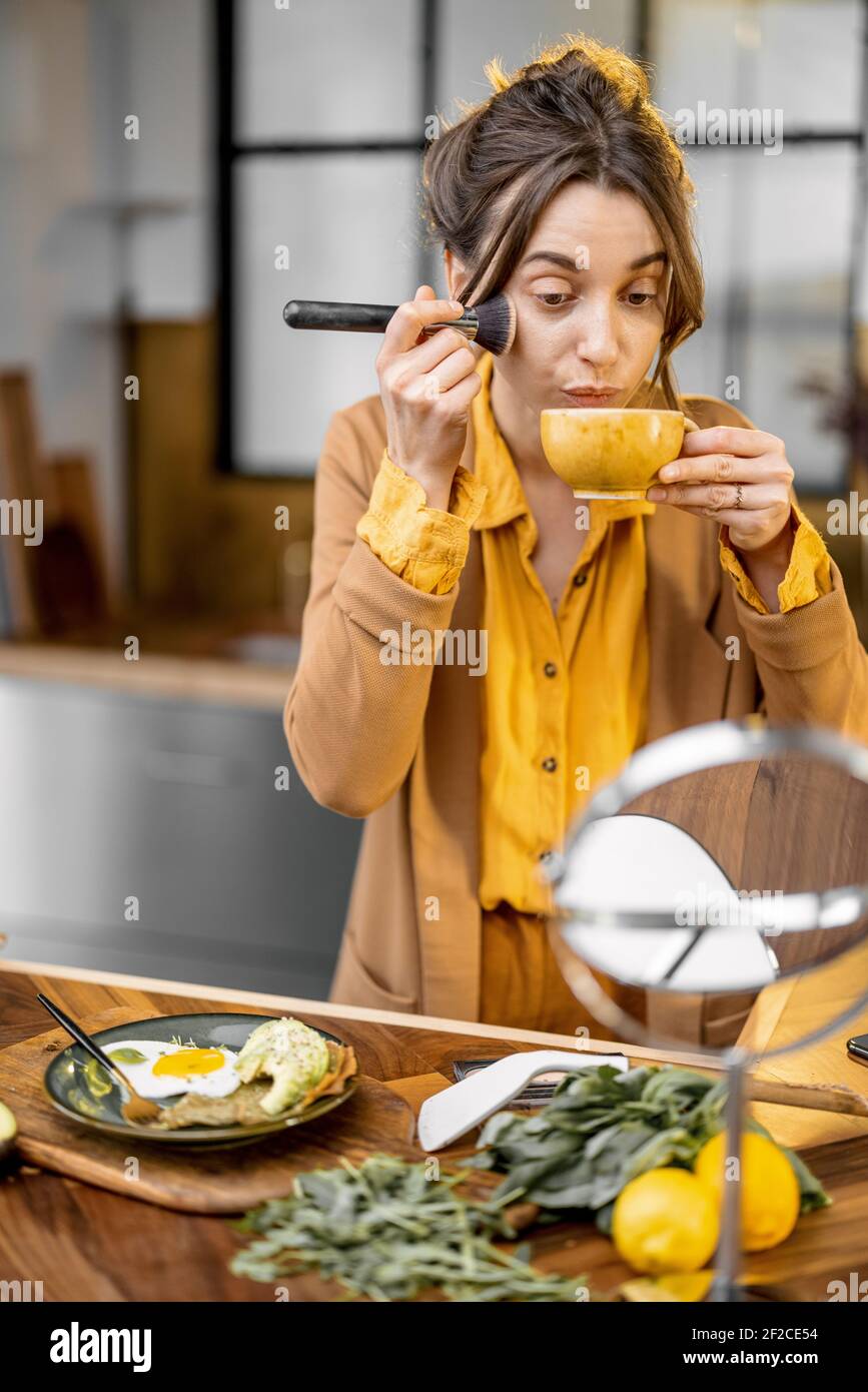 Fussy young businesswoman in a hurry to work in the morning, drinking coffee and apllying makeup on the go Stock Photo