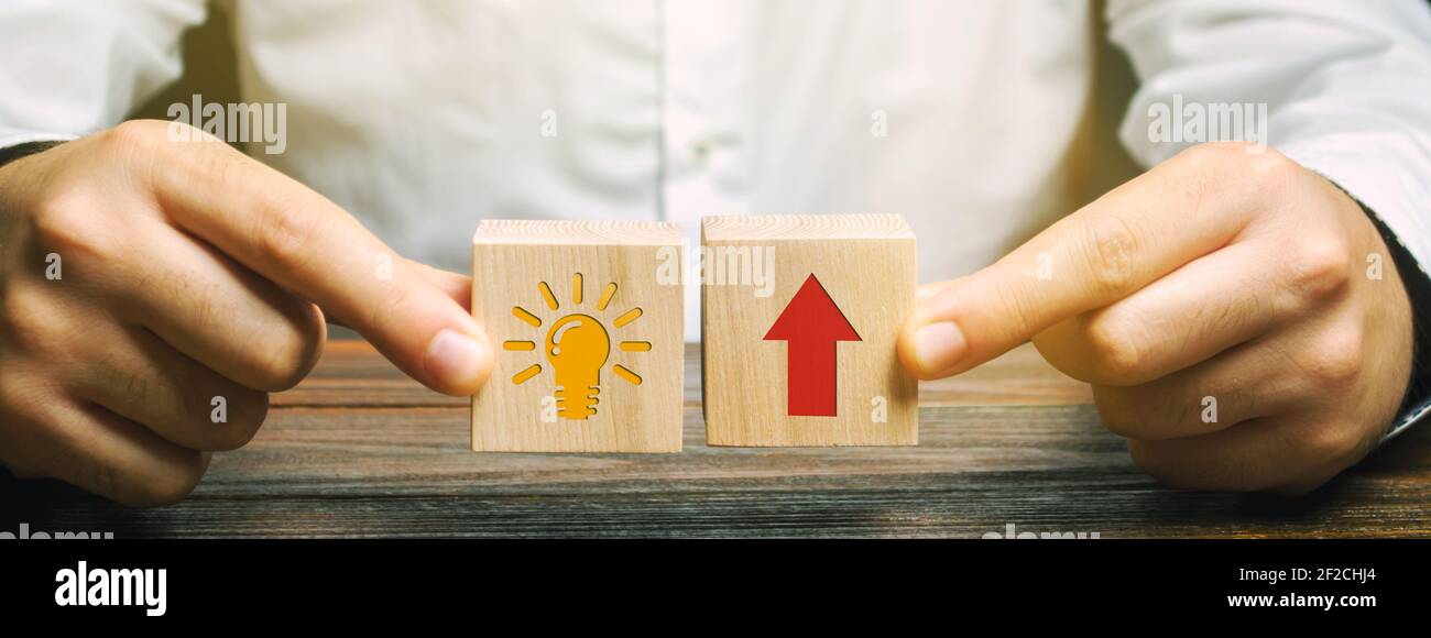 A businessman is holding wooden blocks depicting a business idea and up arrow. Concept of new innovation ideas and discoveries. Vision, planning. Stra Stock Photo