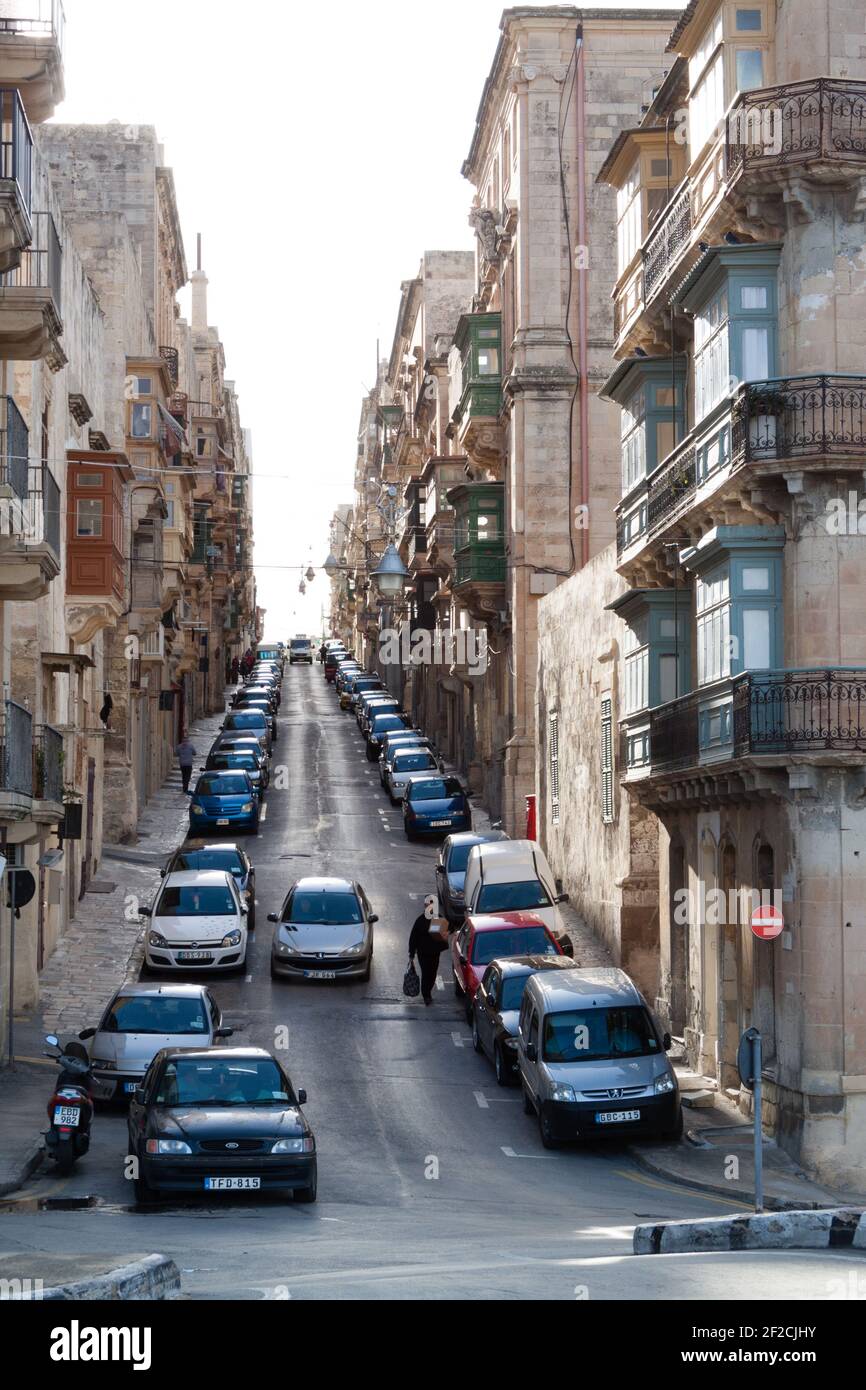 Steep street full with cars leading uphill among sandstone buildings on Valetta, Malta Stock Photo