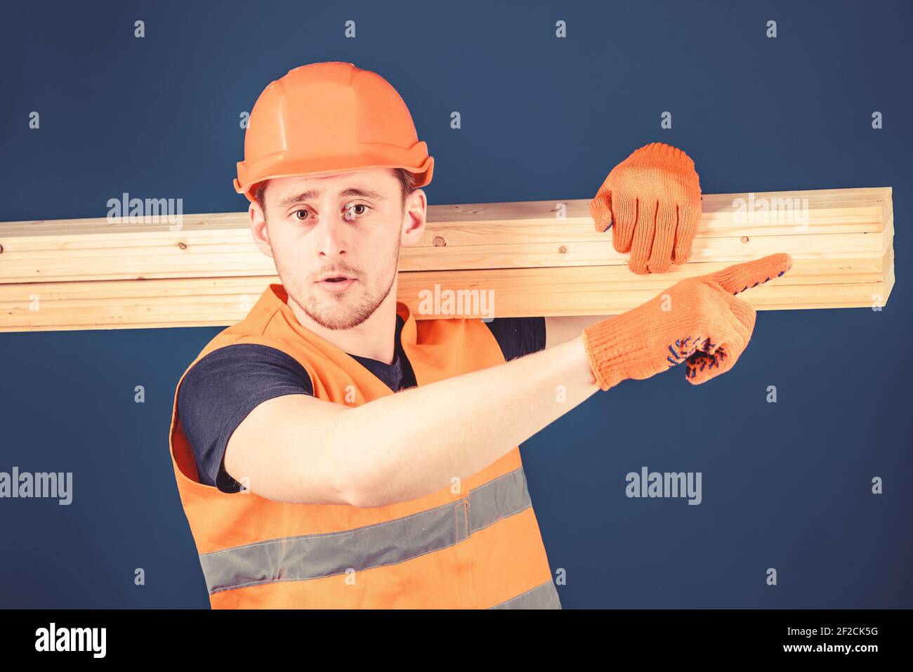 Carpenter, woodworker, strong builder on strict face carries wooden beam on shoulder. Wooden