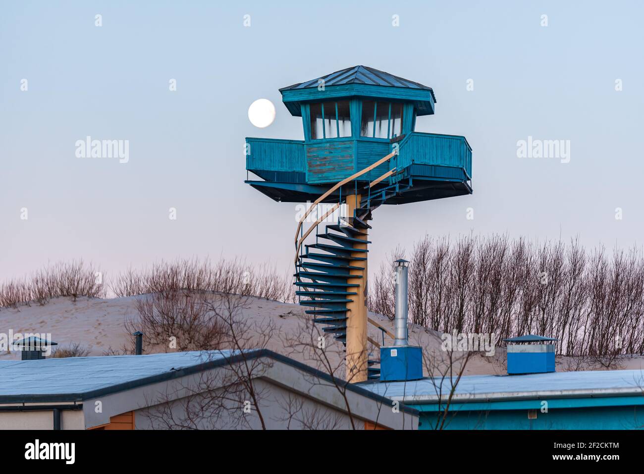 full moon in the morning and a tower for beach rescuers in blue with stairs and beach sand bushes Stock Photo
