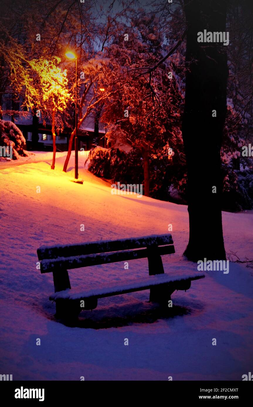Lonely bench in a quiet snowy winter park in the Slovak town Myjava in the evening Stock Photo