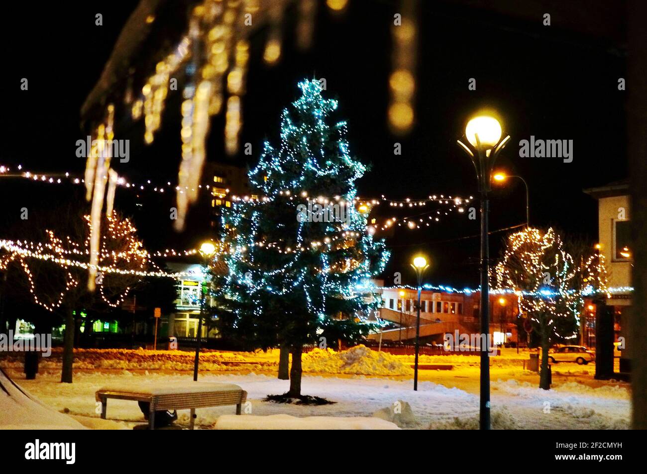 Picture of a beautiful Christmas tree and Christmas lights in the snowy square of a Slovak town Myjava with blurred illuminated icicles in the foregro Stock Photo