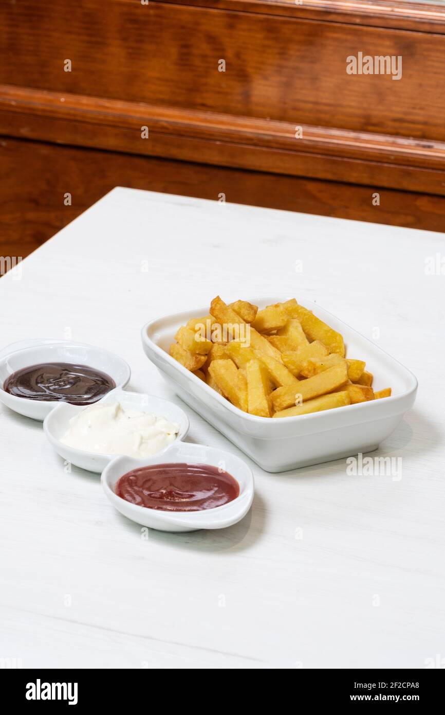 French fries with three dips, barbecue, mayo and ketchup on a table in a restaurant Stock Photo