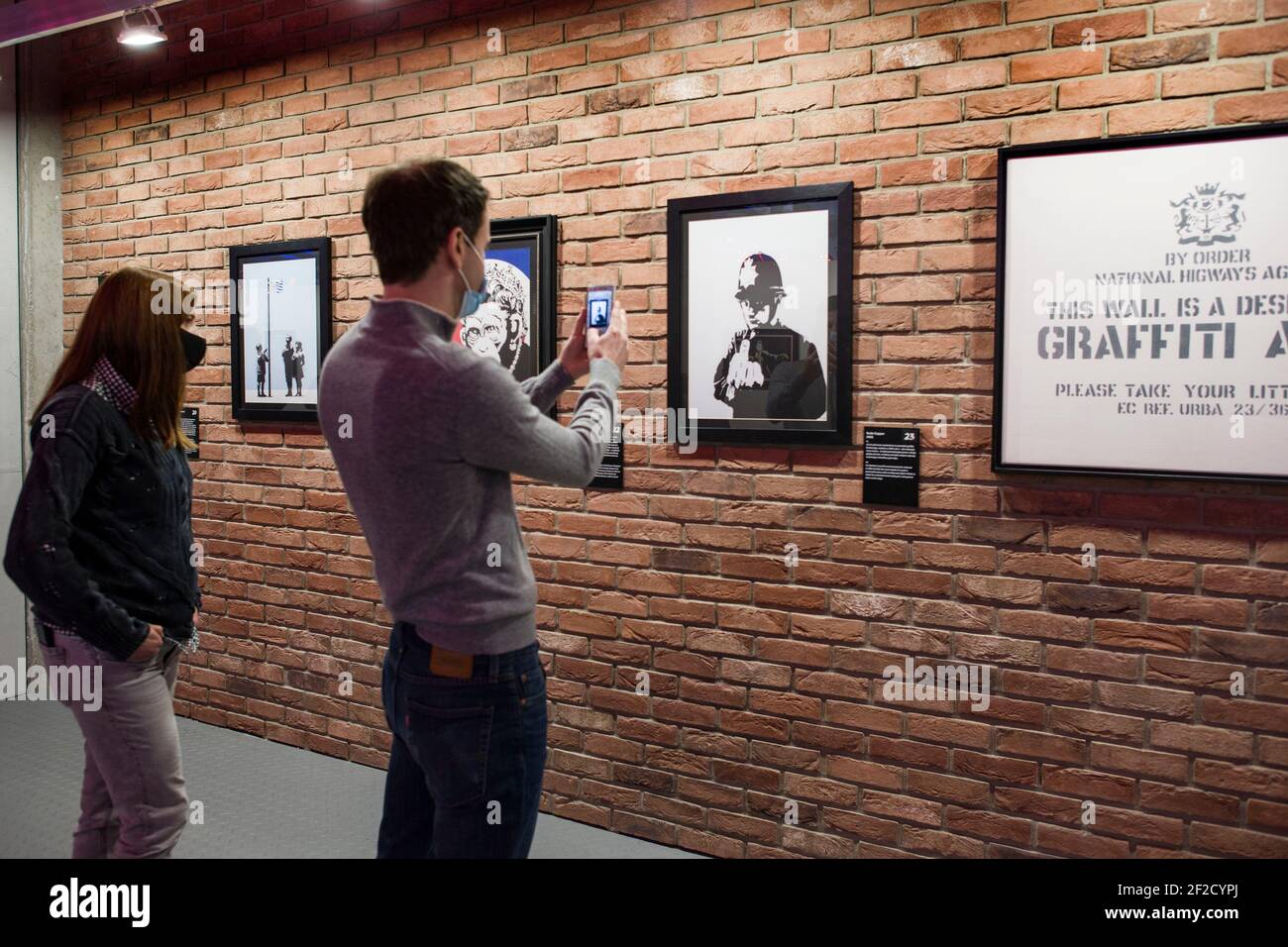 A visitor taking photos with his smartphone of Banksy's work in the gallery during the exhibition.At the Koneser Centrum Praskie gallery 'The Art of Banksy. Without limits” exhibition is the first in Poland as a large presentation of the works of this mysterious artist. It presents over 100 works, original exhibits but also works in the form of photographs, sculptures and many others. Moreover, some of the exhibits are reconstructed using his own technique – templates created especially for this exhibition. AS most of Banksy's exhibition this one is also not authorized by the artist. Stock Photo