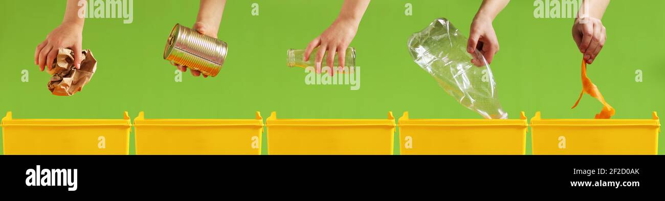 Children's hands throw paper, metal, glass, plastic, organic garbage into different yellow containers on a light green background. Waste sorting. Envi Stock Photo