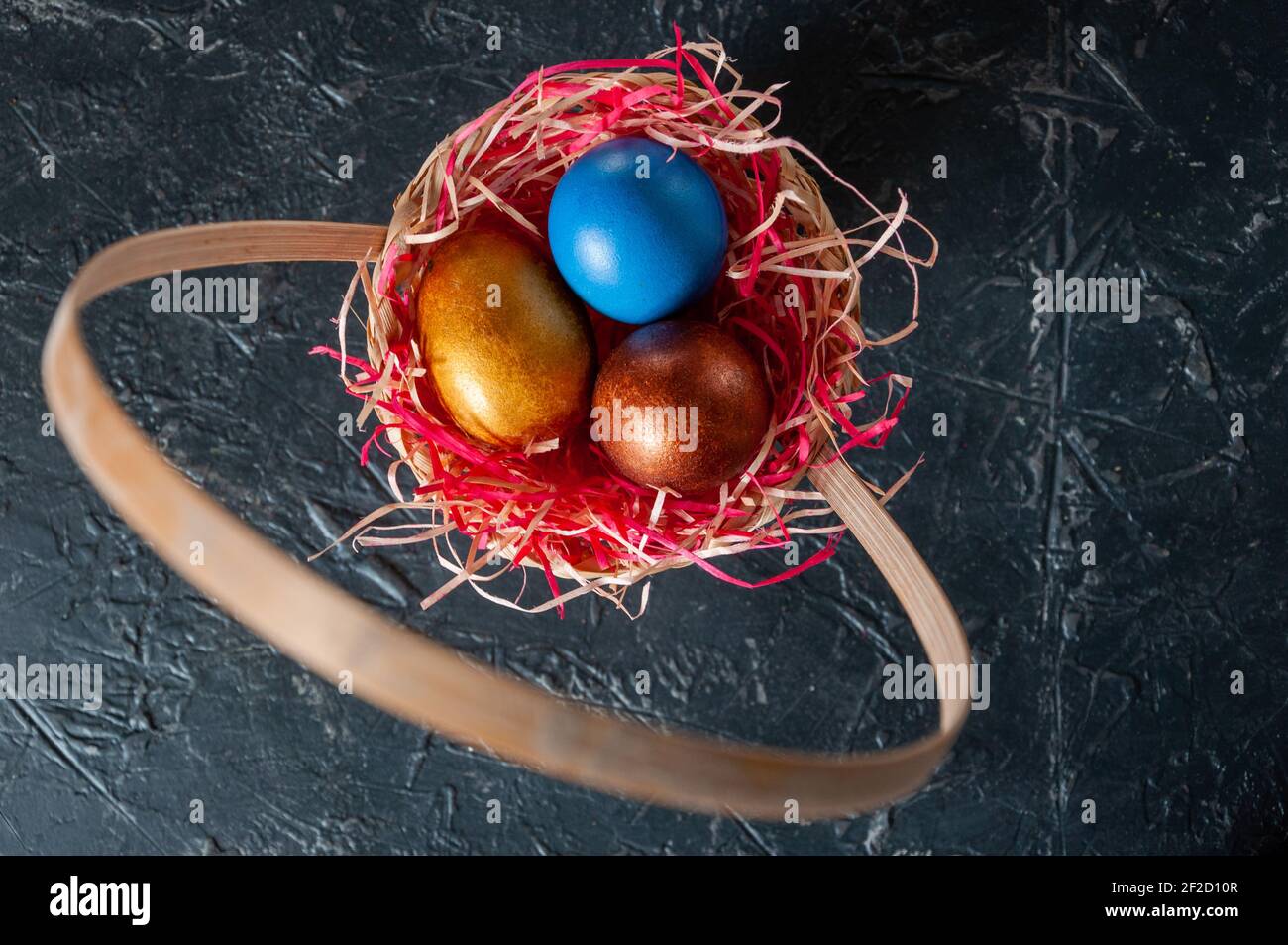 Homemade multicolored painted Easter eggs on colorful straw in a wicker basket on a dark background Stock Photo