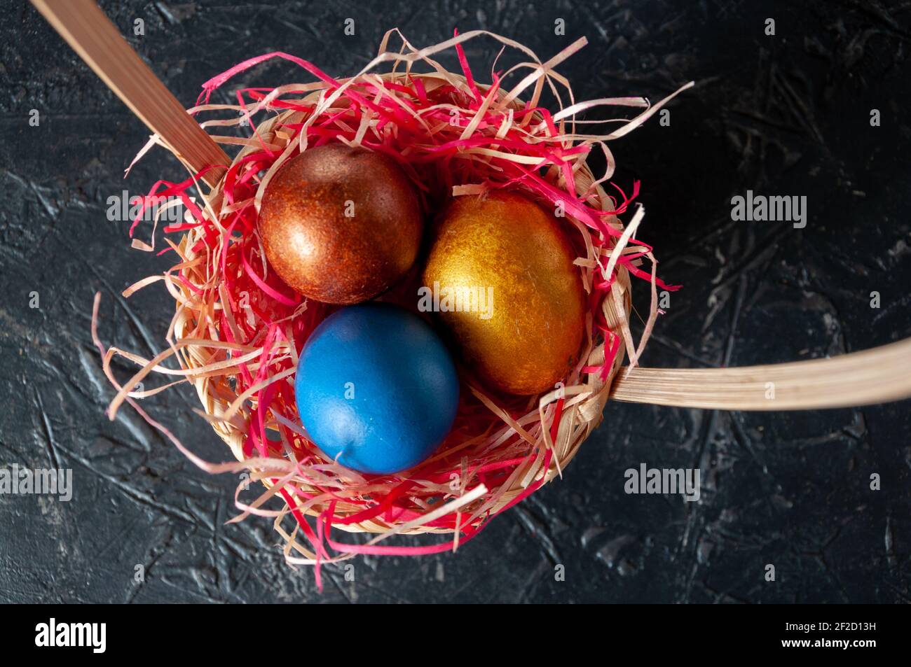 Homemade multicolored painted Easter eggs on colorful straw in a wicker basket on a dark background Stock Photo