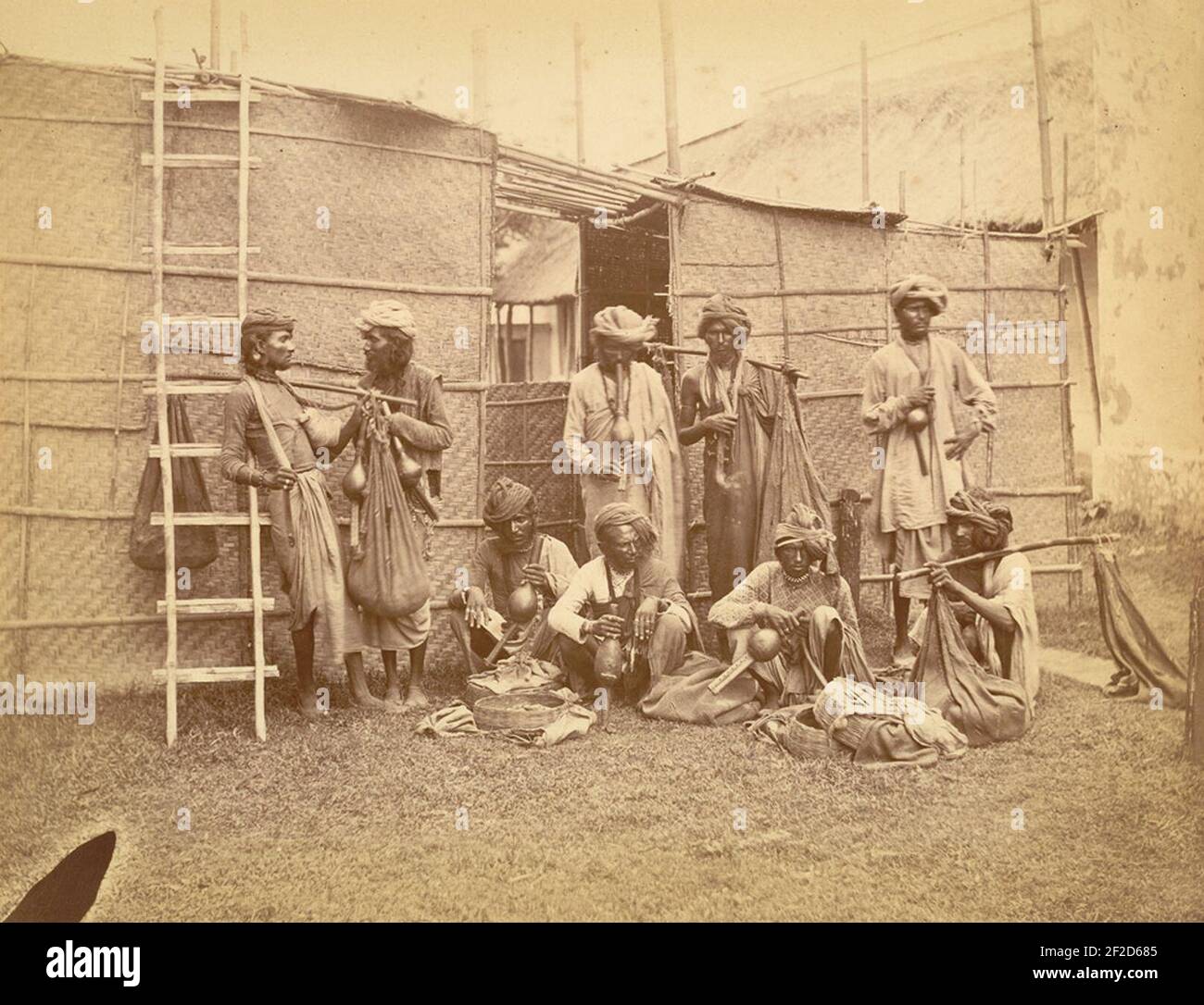 Portrait of 9 snake charmers posed with their pipes, baskets and sacks