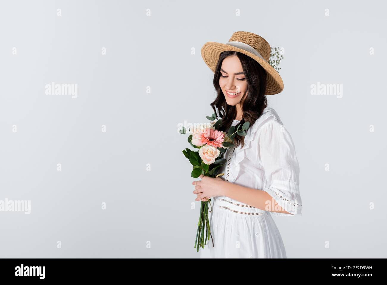 cheerful young woman in straw hat and dress holding bouquet of spring ...
