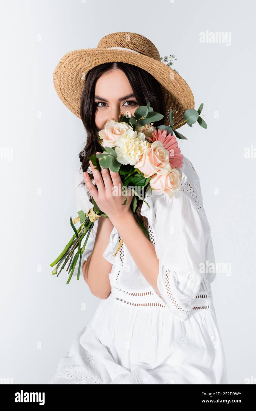young woman in straw hat and dress covering face with bouquet of spring ...