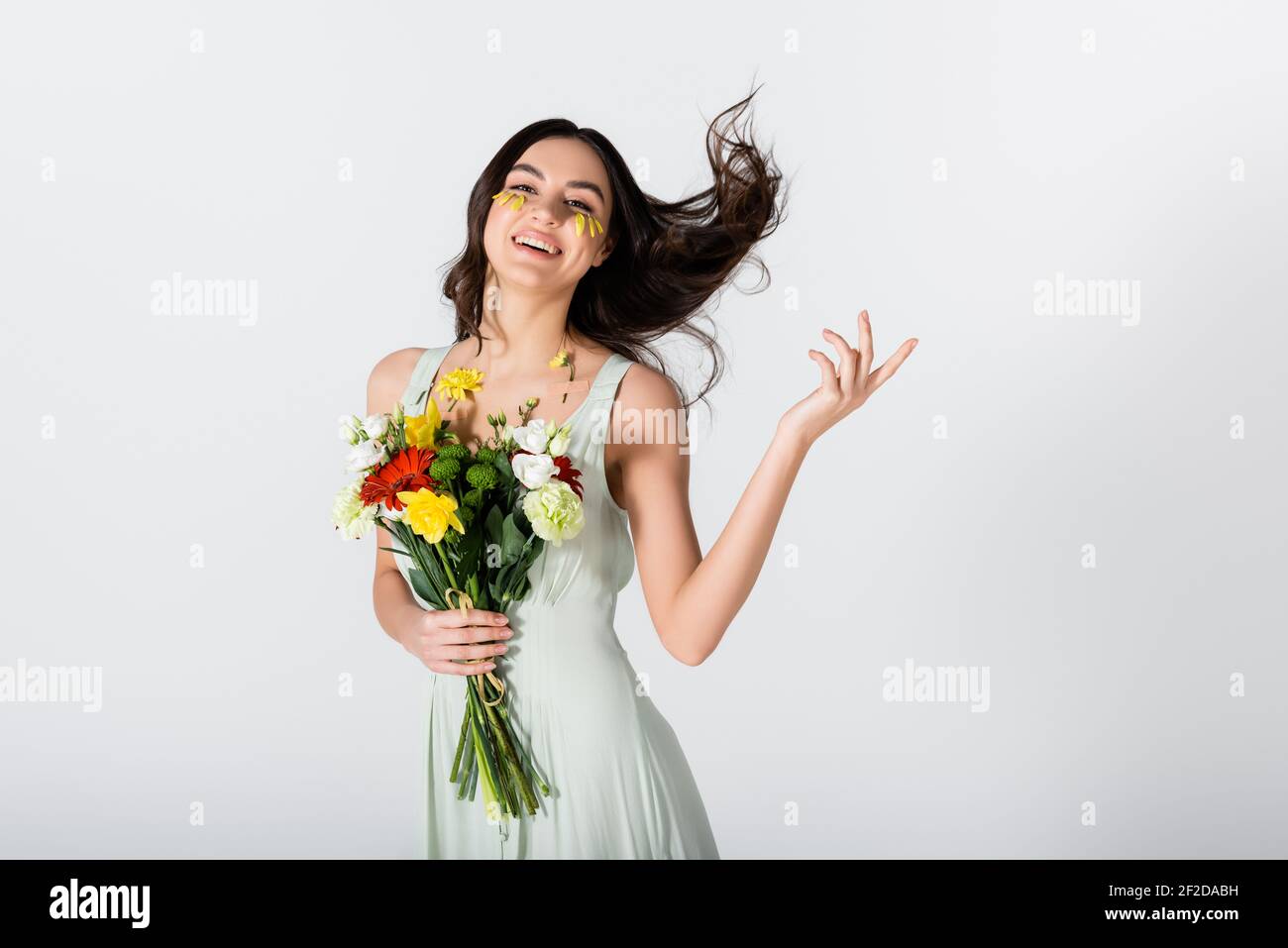 cheerful young woman with petals on face holding bouquet of flowers ...