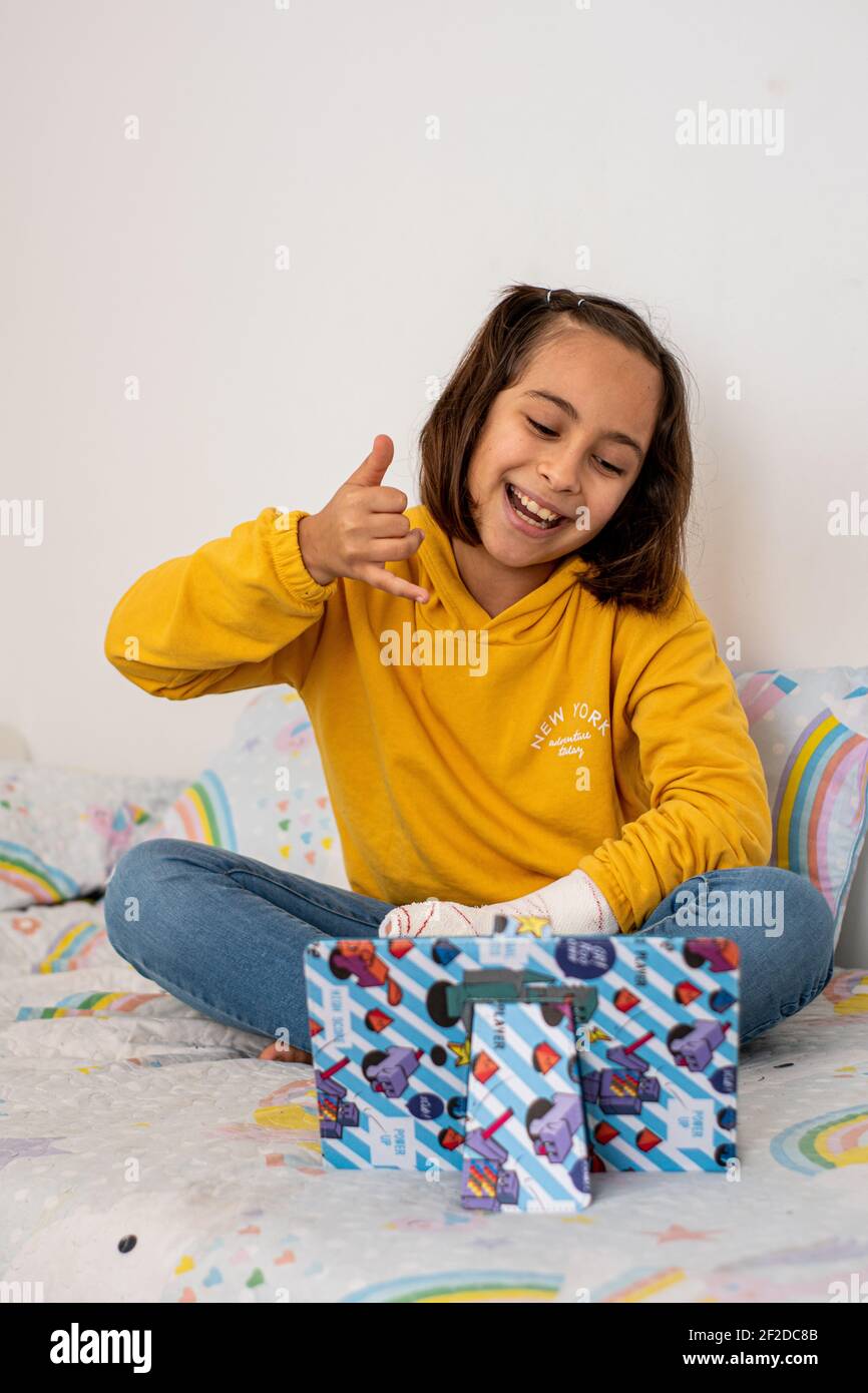 Little Caucasian girl, with a cast in one hand, wearing yellow pullover,  blue jeans and barefoot, making a video call with friends, waving and  showing Stock Photo - Alamy