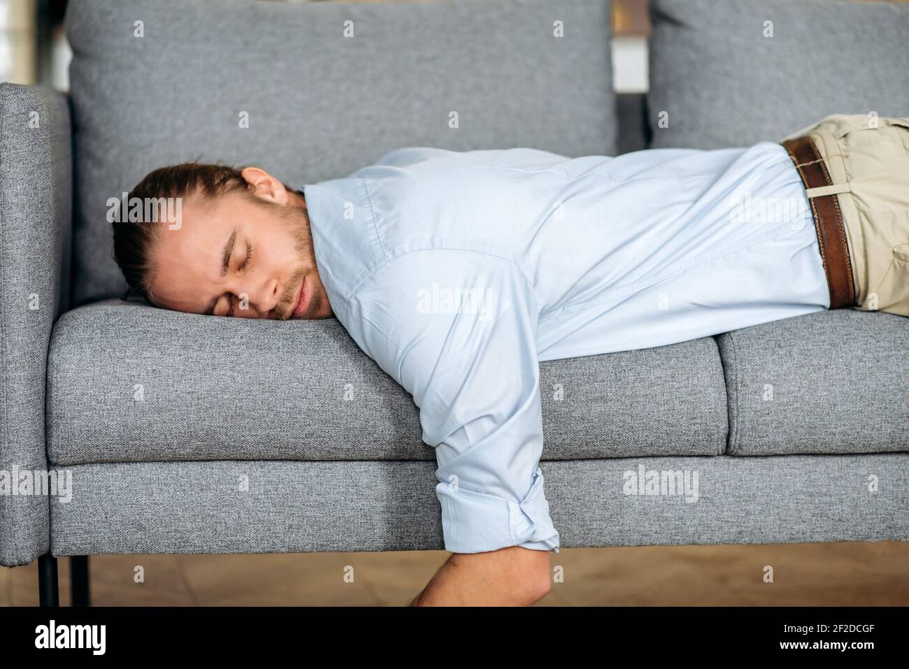 Exhausted tired guy, businessman or student dressed in formal clothes, lying on the couch, tired of work or study, collapsed from fatigue, at home in the living room, need a rest or vacation Stock Photo