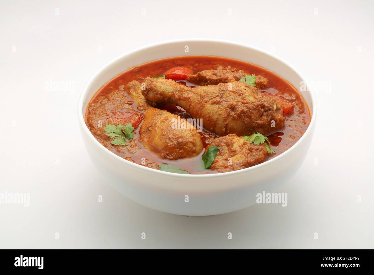 Chicken curry or masala , spicy reddish chicken leg piece dish garnished with coriander leaf and  fresh green chilli which is arranged in a white cera Stock Photo