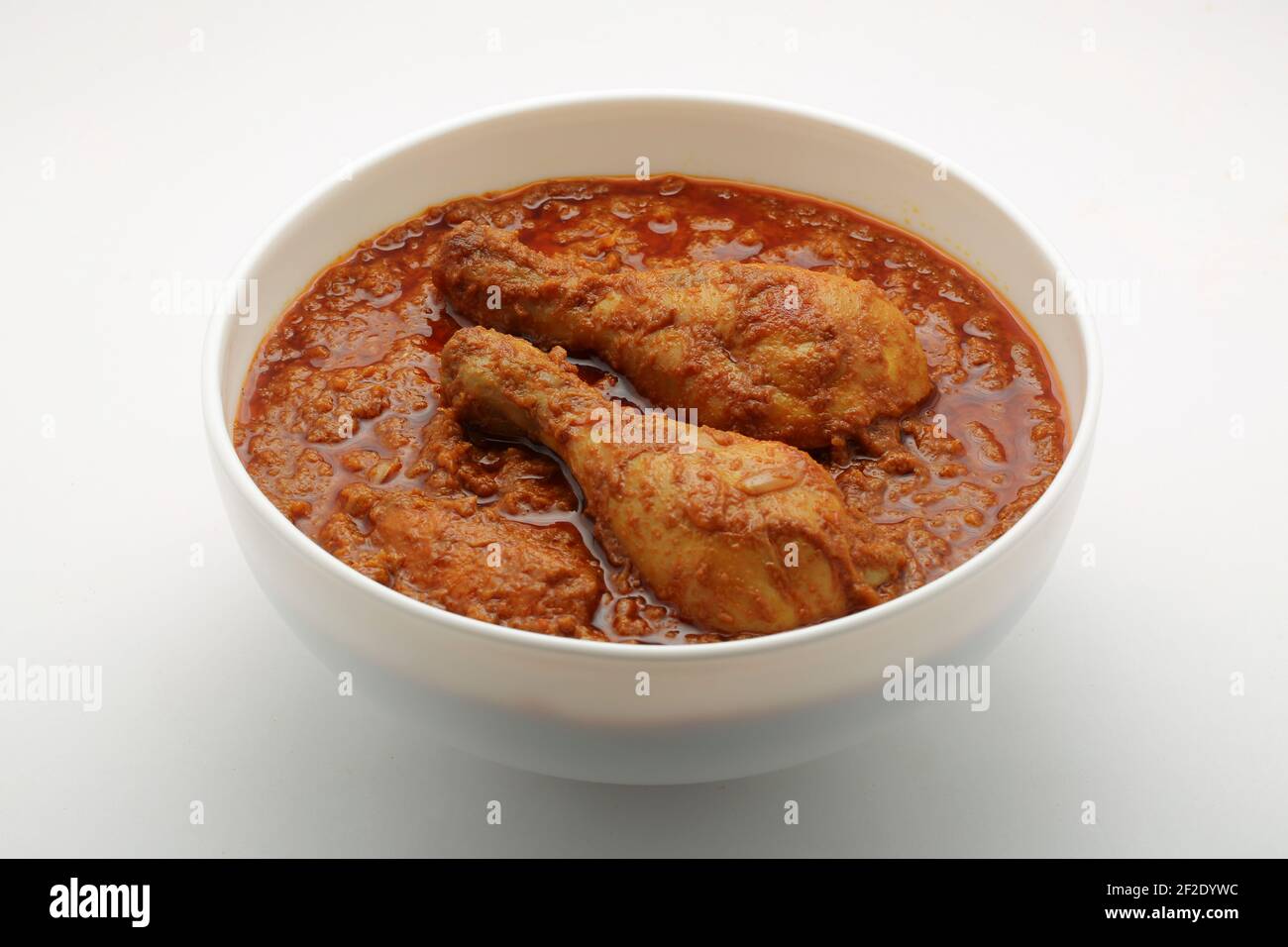 Chicken curry or masala , spicy reddish chicken leg piece dish garnished with coriander leaf and  fresh green chilli which is arranged in a white cera Stock Photo
