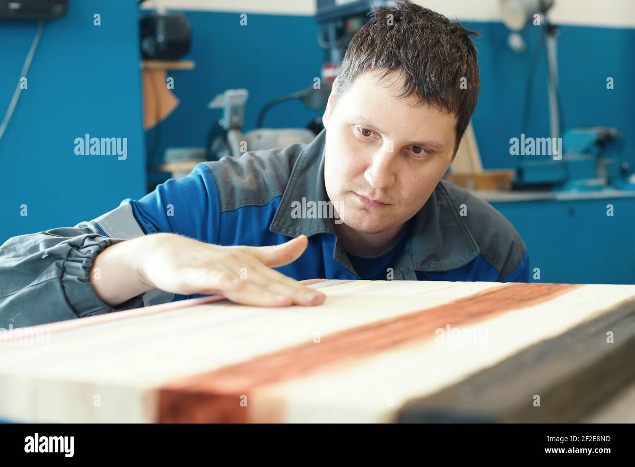 A cabinetmaker works with wood in a carpentry shop. A young worker of Caucasian appearance makes a countertop. Stock Photo