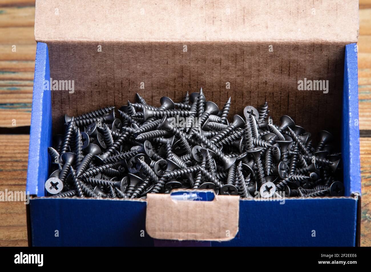 Black screws in a cardboard box. Wooden texture background. Screws for