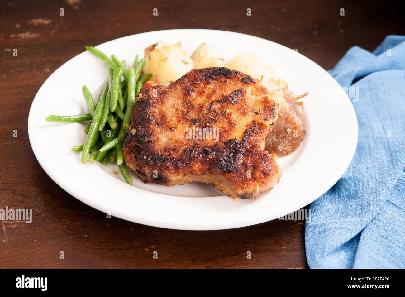 pan searched pork chop breaded with herbs and spices with herb encrusted potato and haricote vert Stock Photo