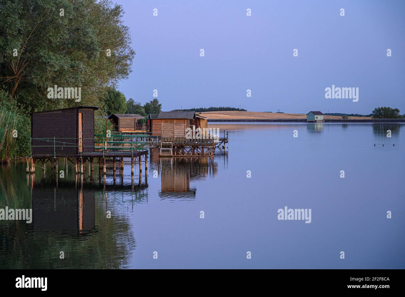 Calm lake water surface and several fishermen's stilt houses. Summer evening at Albe Lacs, Sarreguemines, France. Stock Photo