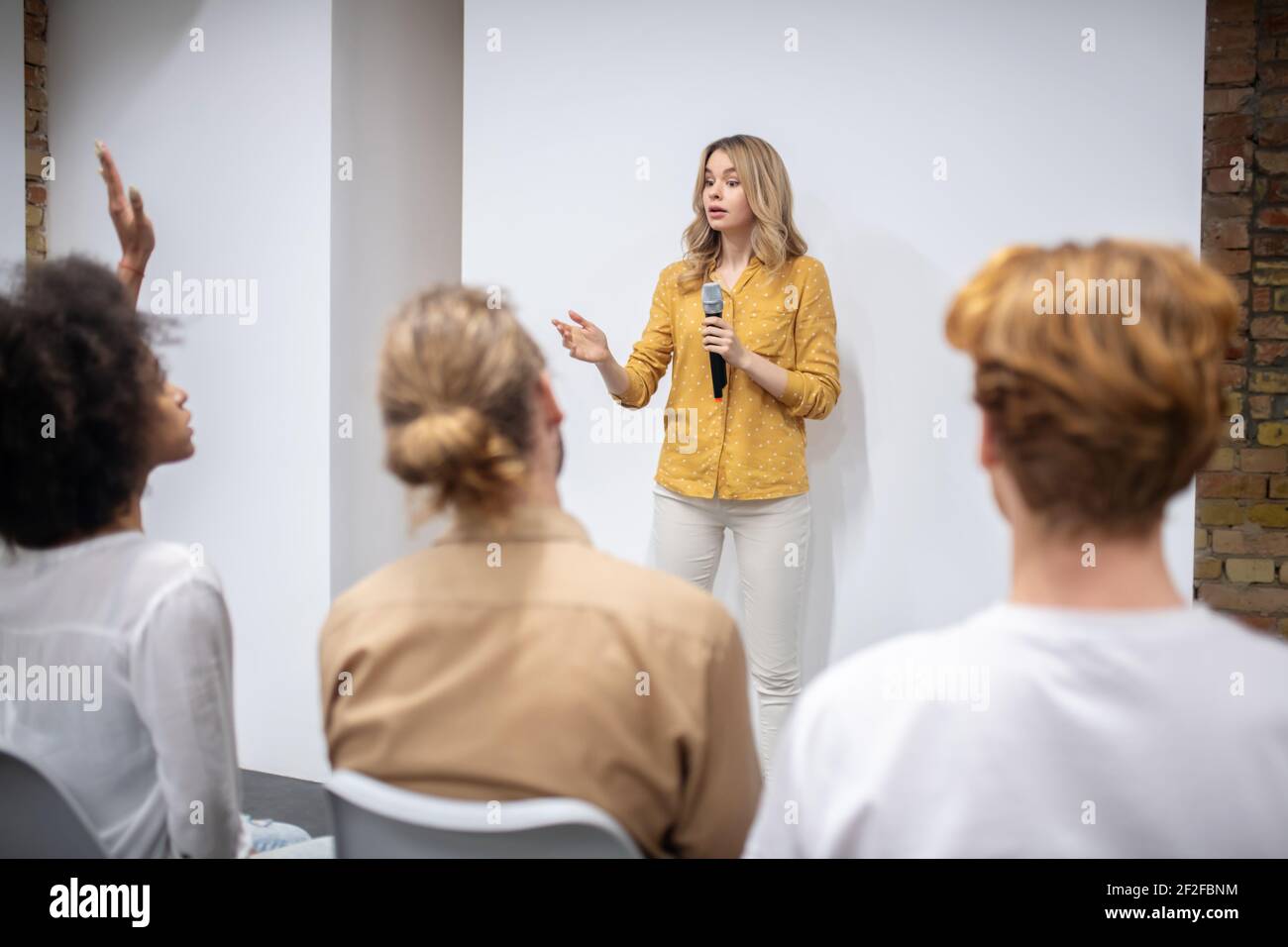 Blonde coach with a microphone talking to the audience Stock Photo