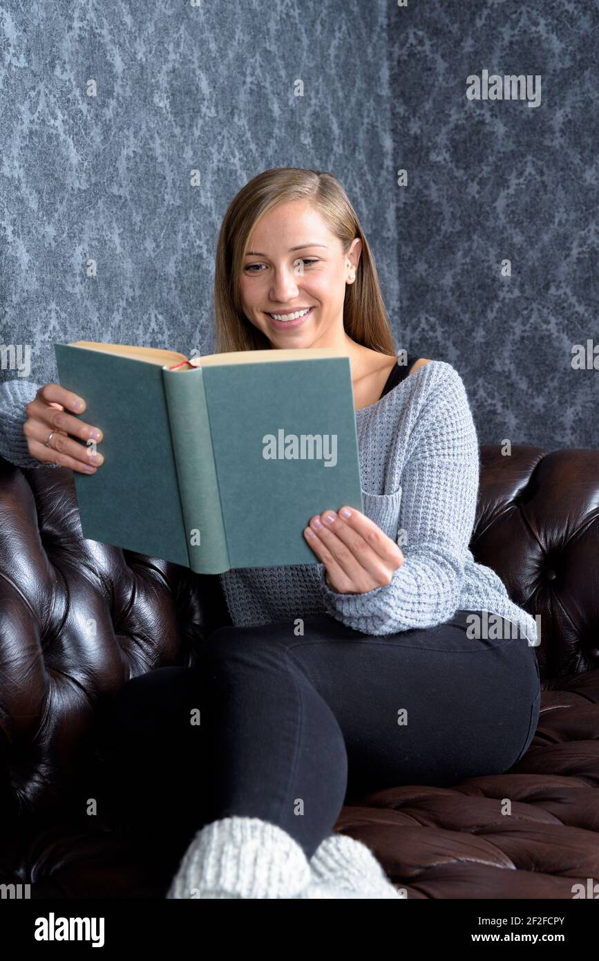 Woman sitting cosy and reads a good book or smiles at lyrics or learns for school Stock Photo