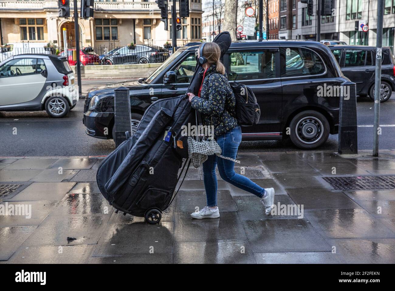 Music Student manoeuvres her cello along Marylebone Road nearby the Royal Academy of Music, Central London, England, United Kingdom Stock Photo