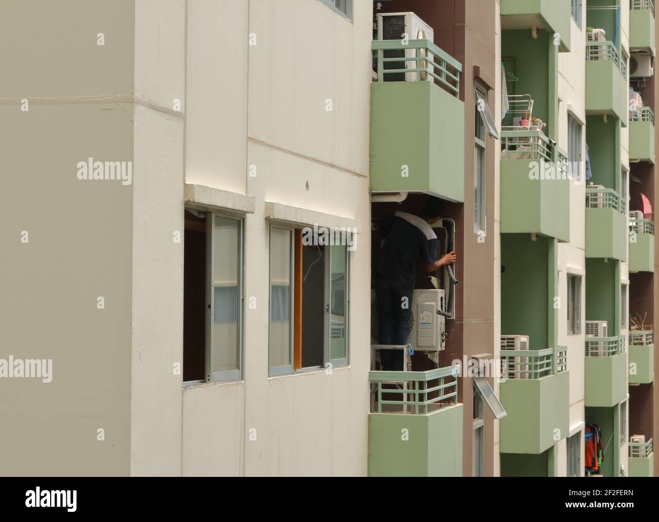 Bangkok, Thailand- March 11, 2021: A technician standing on ladder in balcony while installing refrigerant duct of air conditioning system Stock Photo