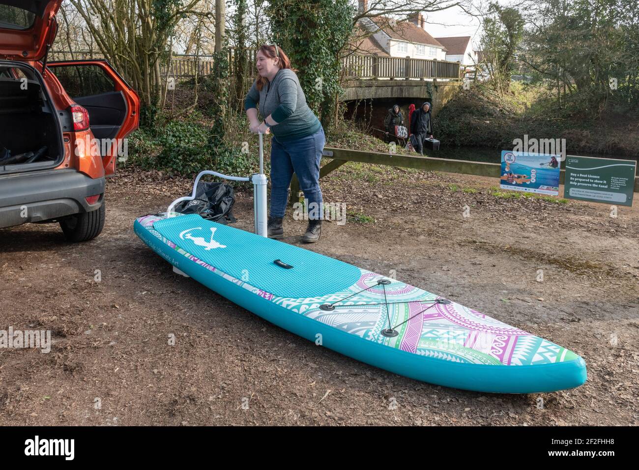 Woman inflating a paddle board (SUP) with a hand pump beside a canal, UK Stock Photo