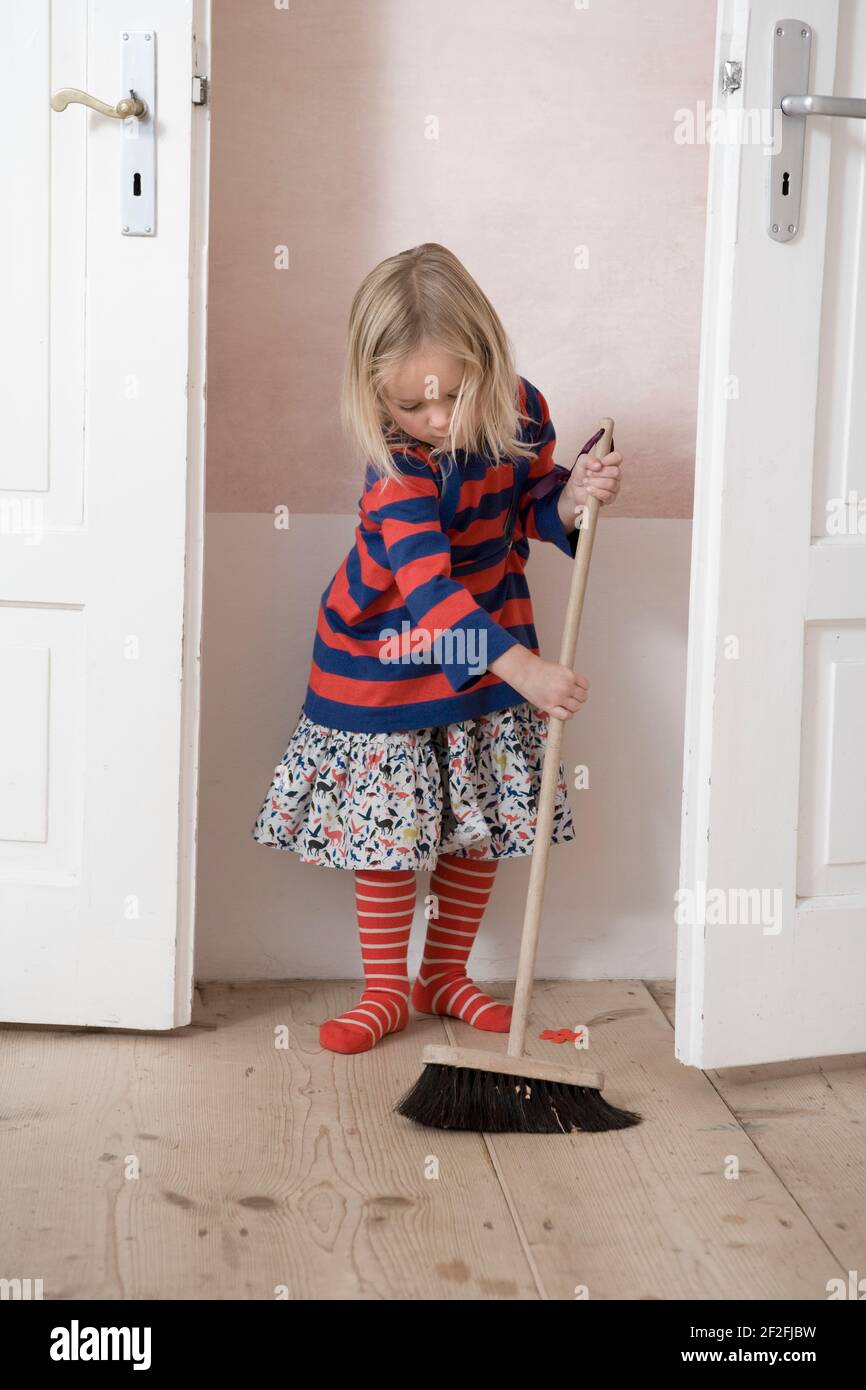 Child sweeps the floor with a broom Stock Photo